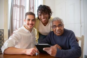 Elderly man enjoying technology with diverse caregivers at home.