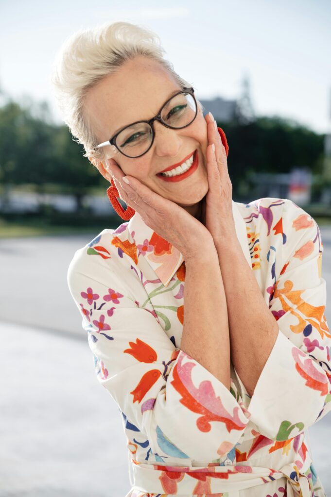 pexels-photo-8417204-8417204 Elderly woman with eyeglasses smiling and posing outdoors in a floral dress.
